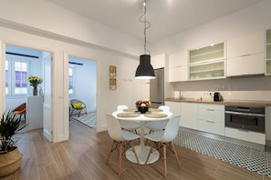 A modern kitchen with white cabinets, a black pendant light, and a dining area with a round table and chairs.