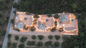 Eine Luftaufnahme eines Resorts mit mehreren Schwimmbecken, die durch Wege verbunden sind, umgeben von Grünflächen und Bäumen.