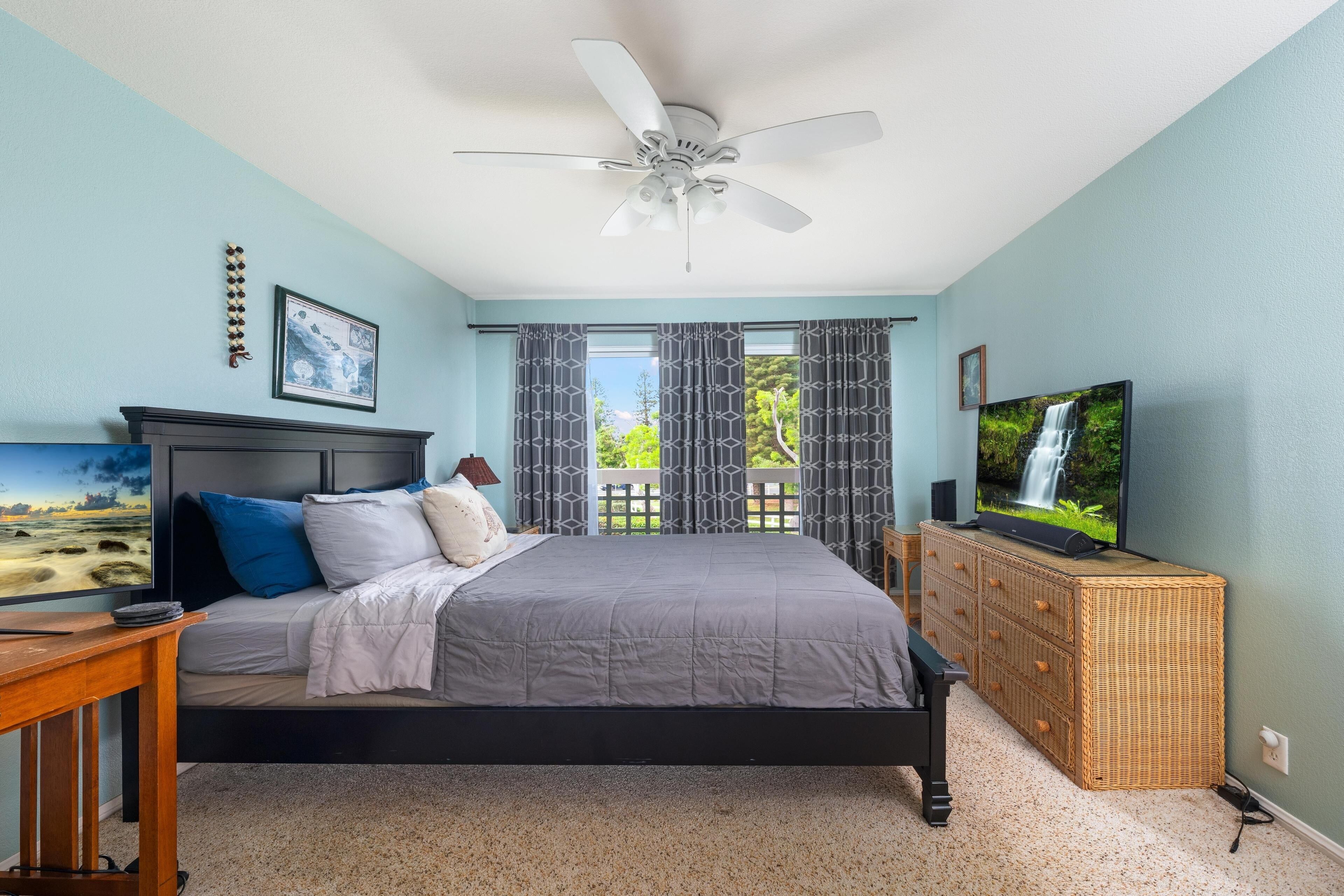 Un dormitorio con cama, ventilador de techo, cómoda, televisor y ventana con cortinas.