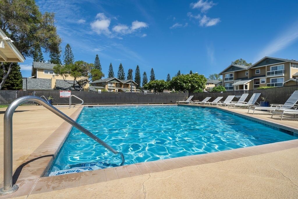 Une piscine avec un escalier en métal, entourée de chaises longues et d’une clôture.