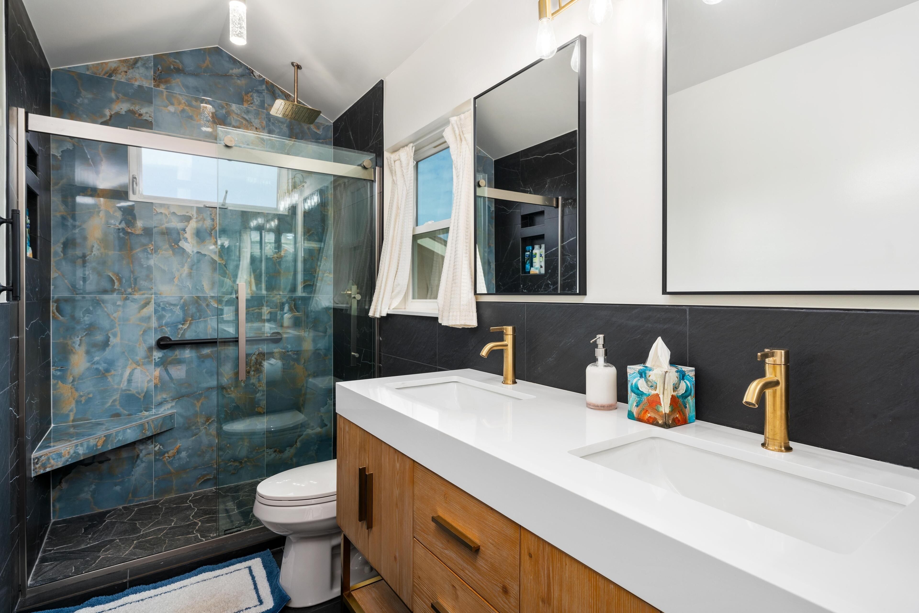 A modern bathroom with a glass shower enclosure, a white sink with gold faucets, and a large mirror.