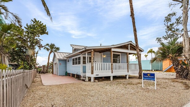 A small, single-story building with a porch, surrounded by gravel and palm trees. - 1030 Second Street 1 Bedroom Home by RedAwning (Fort Myers Beach)
