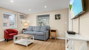 A modern living room with a striped sofa, a red armchair, a wooden coffee table, and a TV on a white stand. - 1030 Second Street 1 Bedroom Home by RedAwning (Fort Myers Beach)