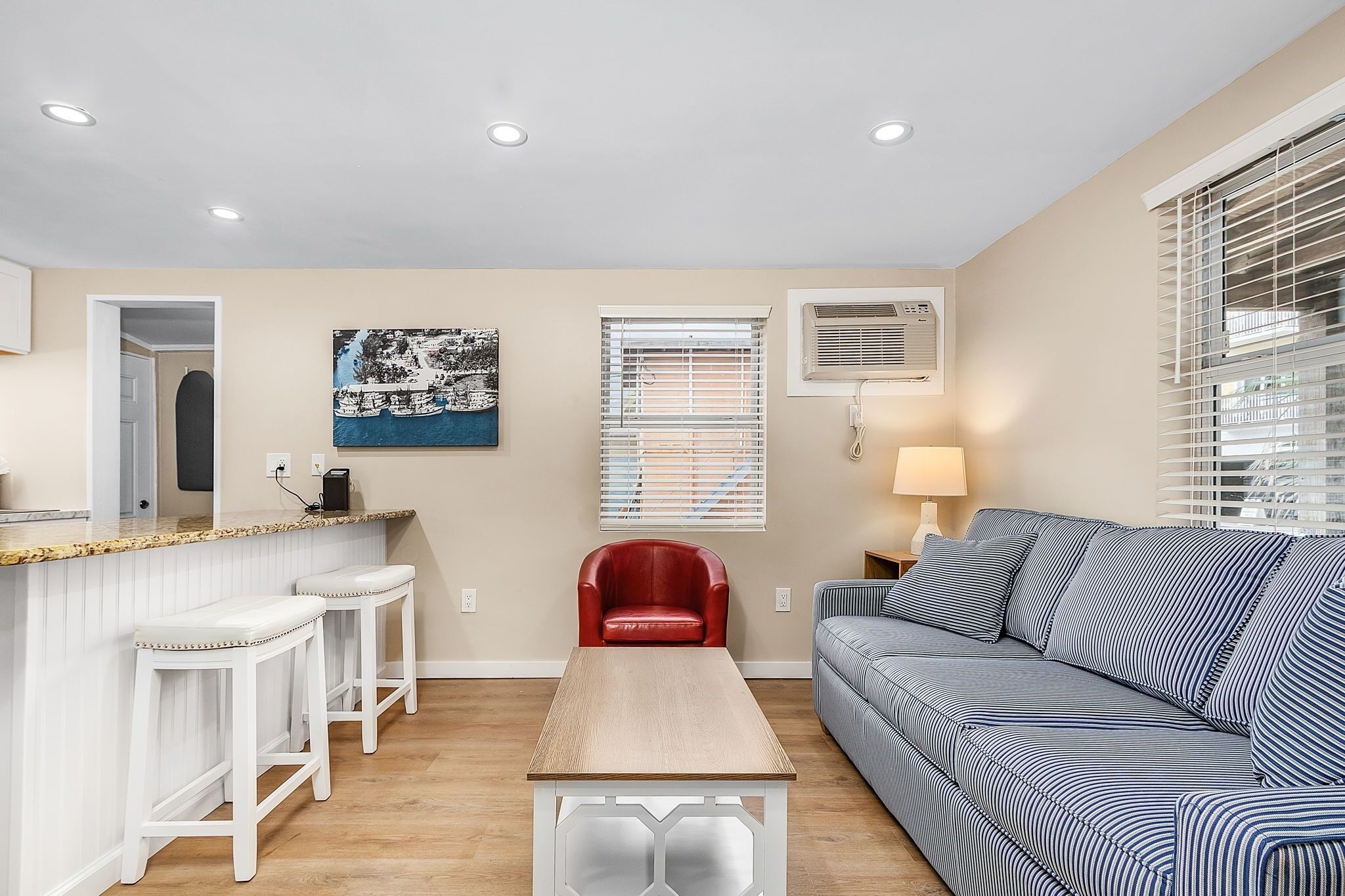 A compact living space with a kitchen area, a red chair, a striped sofa, and a painting on the wall.