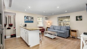 A modern apartment with a kitchen, dining area, and living room. It includes a kitchen island, a dining table, a sofa, and a TV. - 1030 Second Street 1 Bedroom Home by RedAwning (Fort Myers Beach)