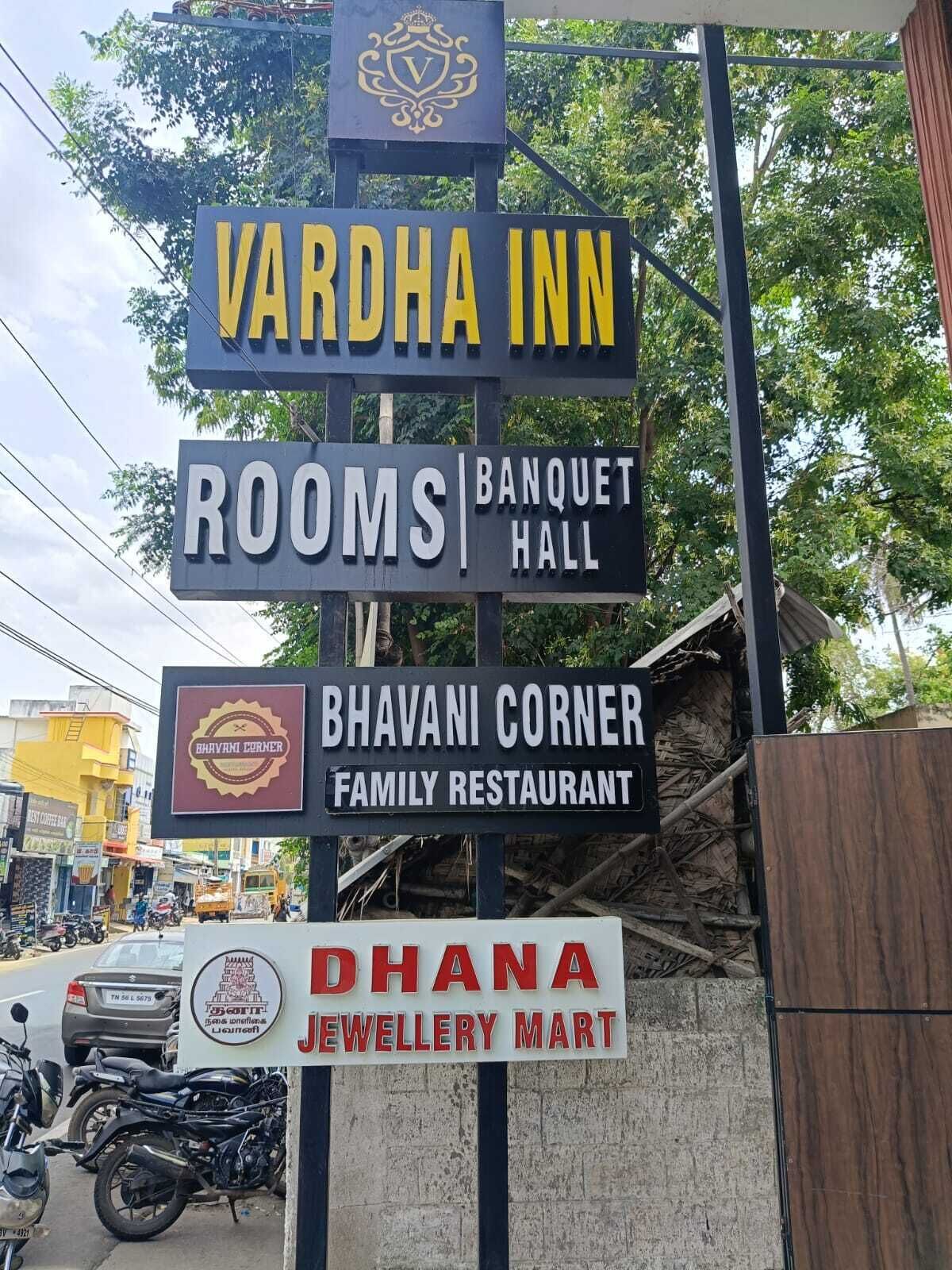 A signboard with multiple business names including Vardha Inn, Rooms, Banquet Hall, Bhavani Corner Family Restaurant, and Dhana Jewellery Mart.