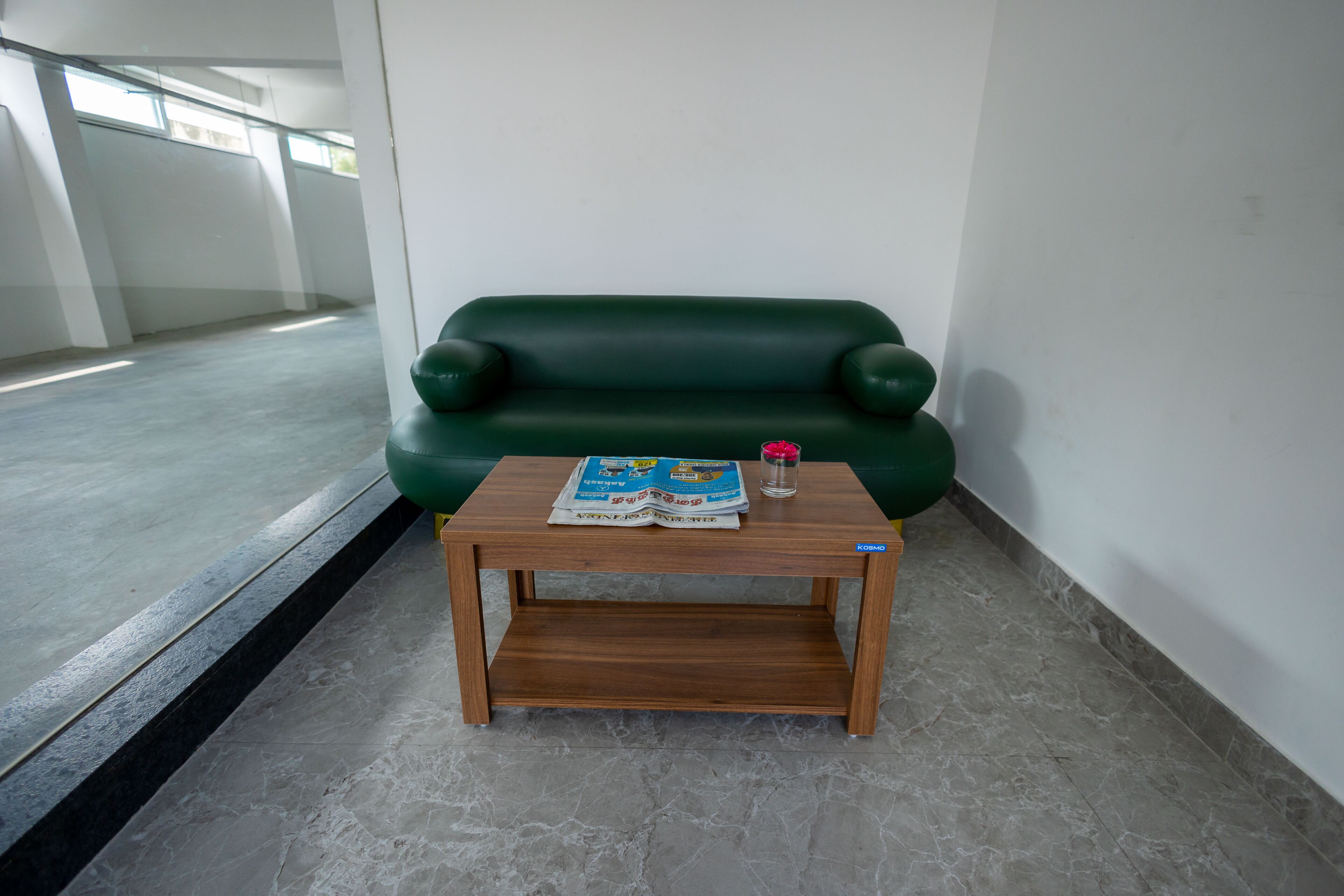 Un sofá verde y una mesa de madera con una revista y un vaso de agua.