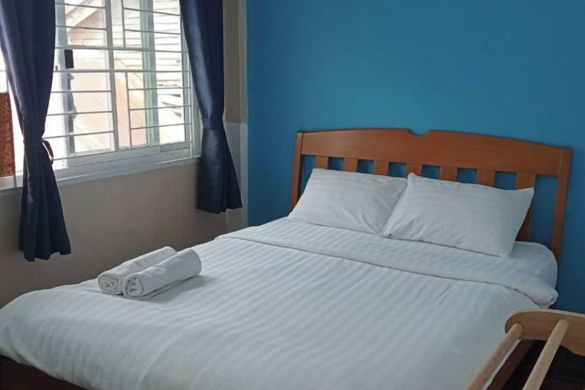 A neatly made bed with white linens and pillows, a wooden headboard, and a window with curtains.