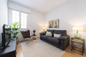 Un salon avec un canapé, deux lampes, un téléviseur et une fenêtre.