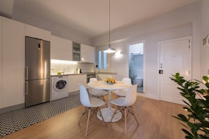 Une cuisine moderne équipée d’un lave-linge intégré, un coin repas avec une table ronde et des chaises, et une porte visible donnant accès à une salle de bain.