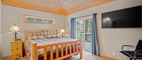 A bedroom with a wooden bed, two bedside tables with lamps, a flat-screen TV, and a view of the outdoors through a window and sliding door.