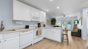 A modern kitchen with white cabinetry, a central island, and a dining area with a bar stool. - Bring your umbrella drinks @Tiki Beach Too! Shipyard 2bed/2bath (Key West)