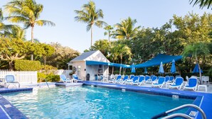 A swimming pool with blue water, surrounded by lounge chairs and umbrellas, and palm trees in the background. - Bring your umbrella drinks @Tiki Beach Too! Shipyard 2bed/2bath (Key West)