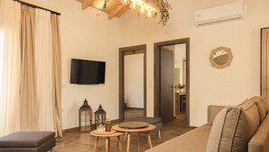 A living room with a sofa, ottoman, small round table, and a flat-screen TV mounted on the wall.