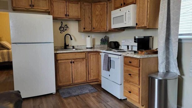 A kitchen with wooden cabinets, a white refrigerator, a microwave, a stove, and a trash can.