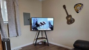 A living room with a flat-screen TV on a stand, a guitar, and a wall decoration.