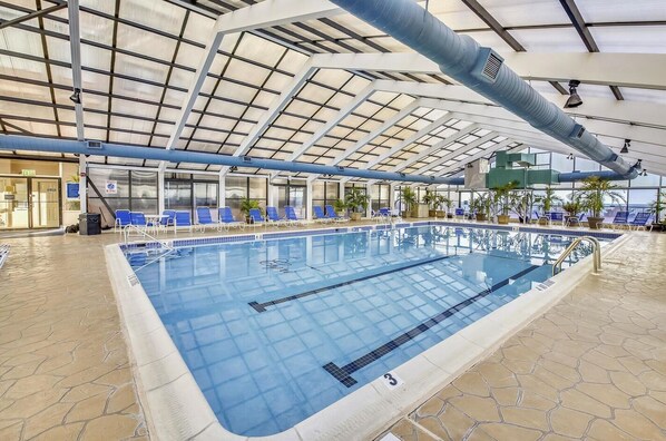 An indoor swimming pool with clear lanes, blue lounge chairs, and a high ceiling with a skylight.