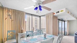 Une chambre d’hôtel dotée d’un coin repas, d’un ventilateur de plafond, de grandes fenêtres et offrant une vue sur la ville.
