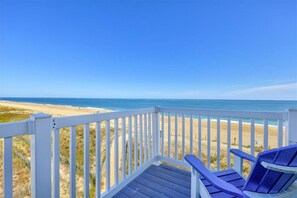Eine Holzterrasse mit weißen Geländern und Blick auf einen Strand.