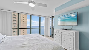 Ein Schlafzimmer mit einem großen Bett, einer weißen Kommode, einem Deckenventilator und einem an der Wand befestigten Fernseher.