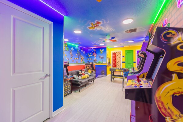 Ein hell erleuchteter Raum mit Spielautomaten, einer Couch mit Kuscheltieren und einer Tür links.