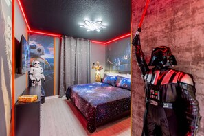 Ein Schlafzimmer mit einem Bettbezug im Weltraum-Design, einer Star Wars Actionfigur und einem Wandbild zum Thema Star Wars.
