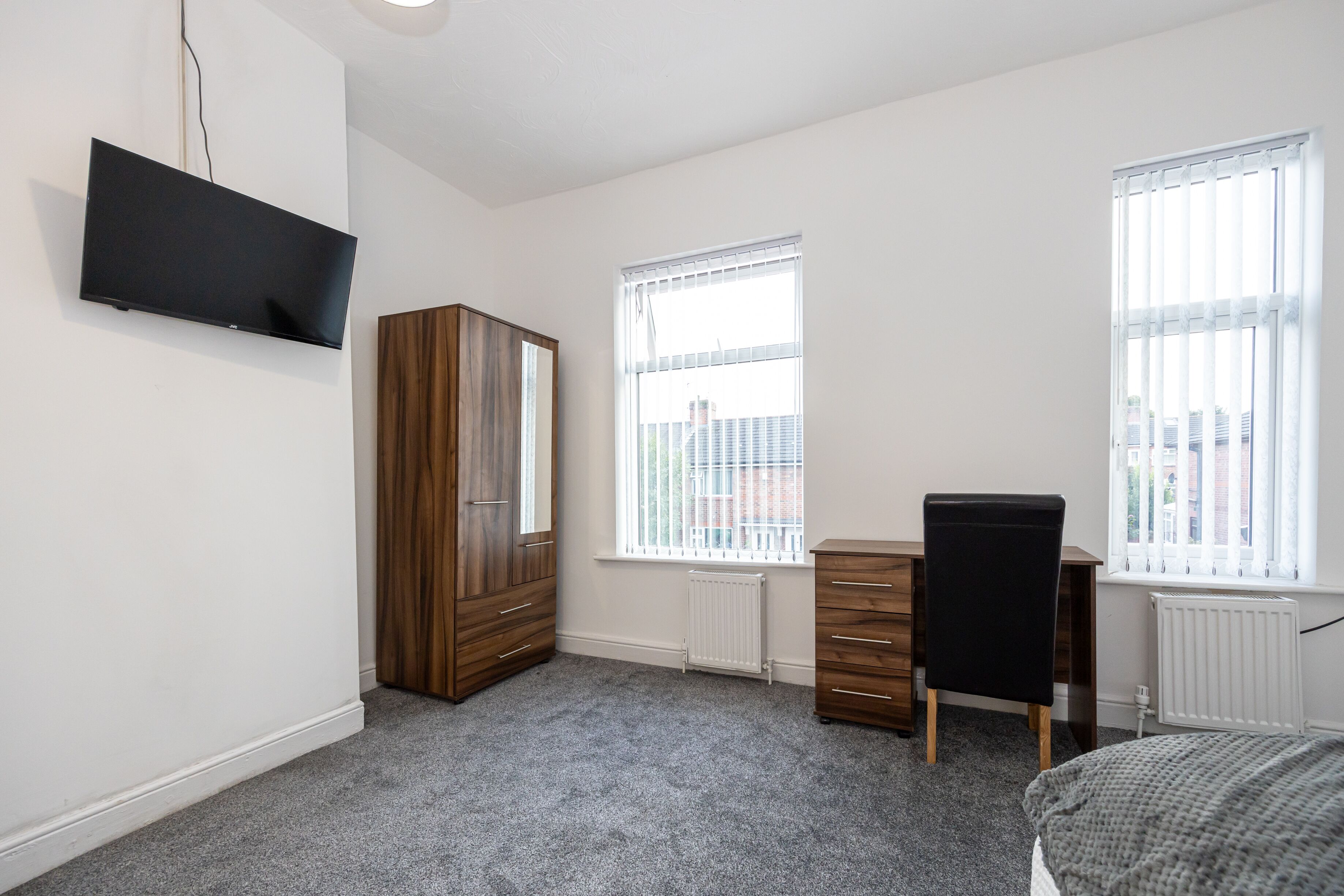 A room with a bed, a desk, a chair, a wardrobe, and a TV mounted on the wall.