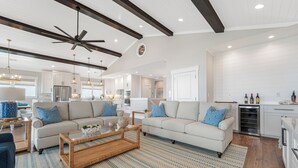 A spacious living room with a large sofa, a coffee table, and a ceiling fan. - New 8BR/7.5BA with Spectacular Ocean View, Elevator, Private Heated Pool (Ocean Isle Beach)
