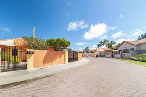 A residential street with houses, a gated entrance, and a clear sky.