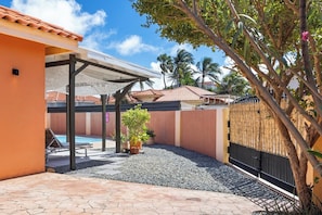 A covered outdoor area with a pool, surrounded by a fence and palm trees. - Private Pool! 3BR Home w Patio near Beaches, Aruba (Noord)