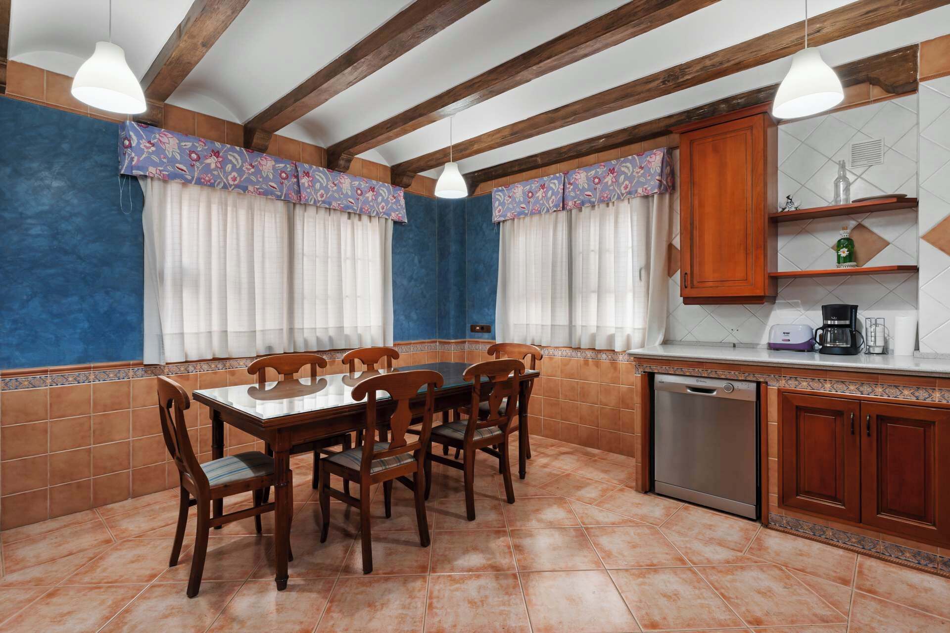Un comedor con mesa y sillas de madera, una cocina con armarios de madera y un lavavajillas.