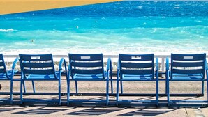 Ein Strand mit blauen Stühlen und freiem Blick auf das Meer.