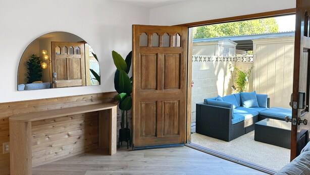 Een kamer met een houten bank, een grote spiegel en een schuifdeur naar een buitenruimte met een blauwe bank en een rieten tafeltje.