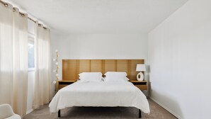 Een slaapkamer met een groot bed, houten hoofdbord, nachtkastjes met lampen en een stoel.