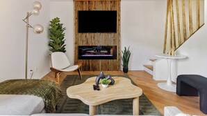 Een moderne woonkamer met een flatscreen televisie, een wand van houten latten, een ronde salontafel, een witte stoel en een trap.