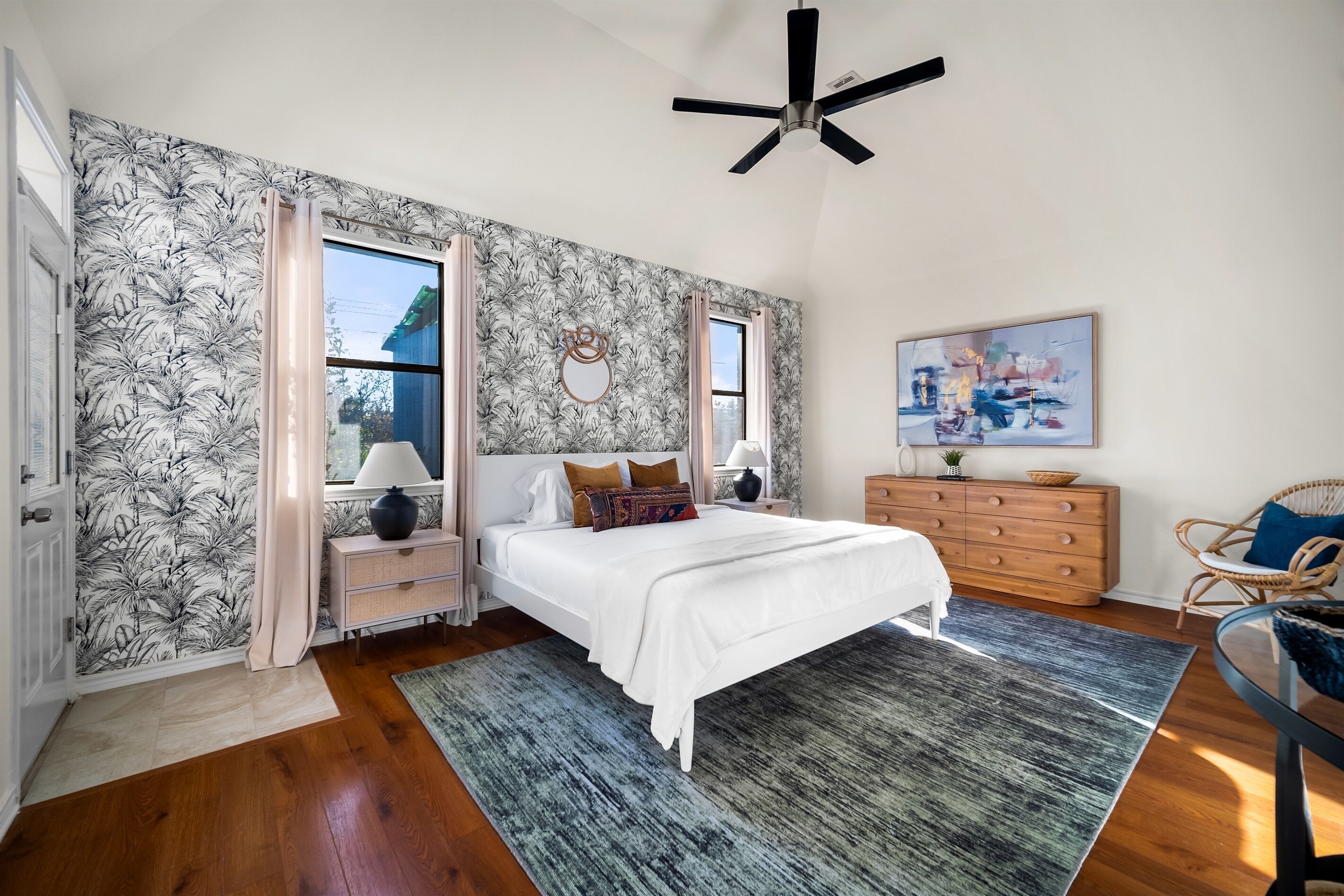 A bedroom with a large bed, a nightstand, a dresser, a chair, and a ceiling fan.