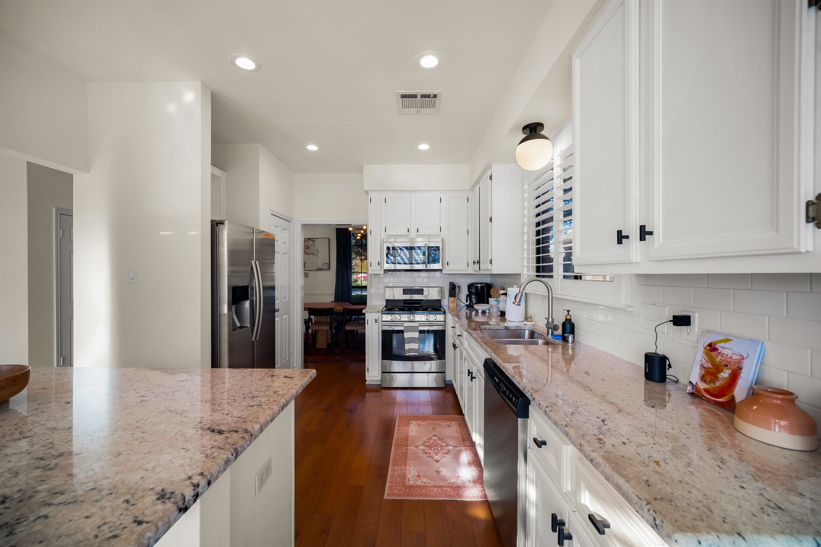 A modern kitchen with white cabinetry, granite countertops, stainless steel appliances, and a central island.