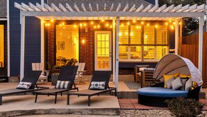 A covered patio area with lounge chairs and a seating area, featuring a pool and a pergola with string lights.