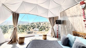 Um quarto amplo com uma cama grande, vista para a paisagem e estrutura no teto com design geométrico.