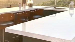 Uma cozinha moderna com bancada branca, banquetas e vista para as montanhas.