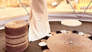 Uma pessoa vestida de branco em pé dentro de uma estrutura em forma de cúpula geométrica, com vista para uma paisagem desértica.