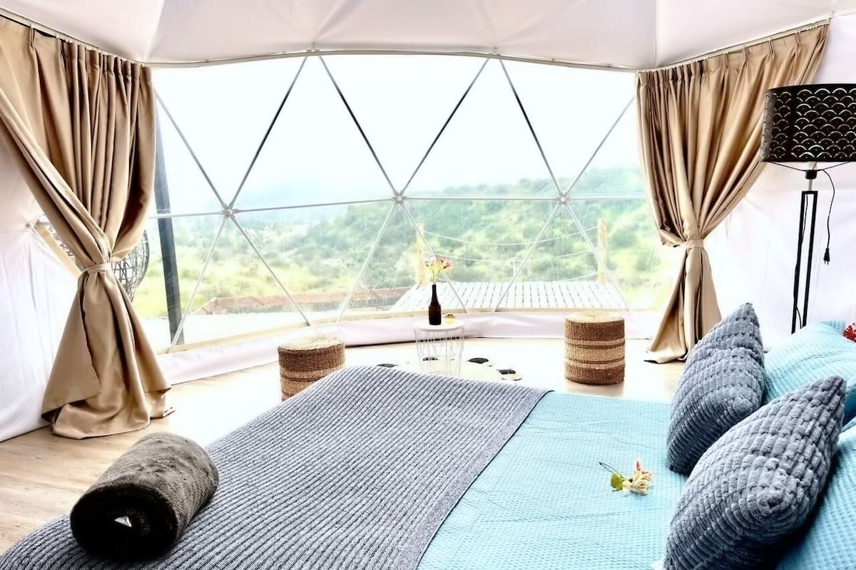 A bedroom with a large bed, a view of the outdoors, and a speaker on a stand.
