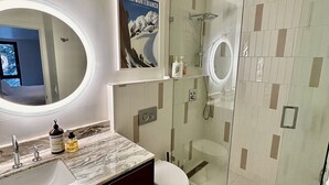 Een moderne badkamer met een marmeren aanrechtblad, een grote spiegel, een douchecabine van glas en een poster aan de muur.