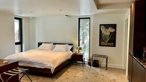 Een moderne slaapkamer met een groot bed, een bureau en een stoel. Er is een raam met uitzicht op bomen en een poster aan de muur.