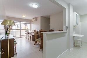 Una sala moderna con un sofá, sillones, una zona de comedor con mesa y sillas, y una cocina con mostrador y armarios.