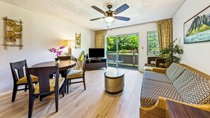 Ein modernes Wohnzimmer mit Deckenventilator, Essbereich mit Tisch und Stühlen, Sofa und Fernseher.