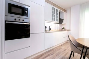 A modern kitchen with white cabinetry, a built-in oven, and a dining area with a table and chairs.