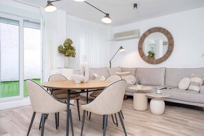 A modern living room with a round dining table, beige chairs, a grey sofa, and a round mirror on the wall.