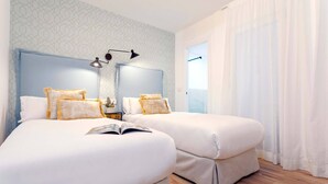A hotel room with two beds, a nightstand, a lamp, and a window with curtains.