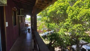 Un porche cubierto con un banco, un árbol y vista a un patio trasero con un coche y una bicicleta.